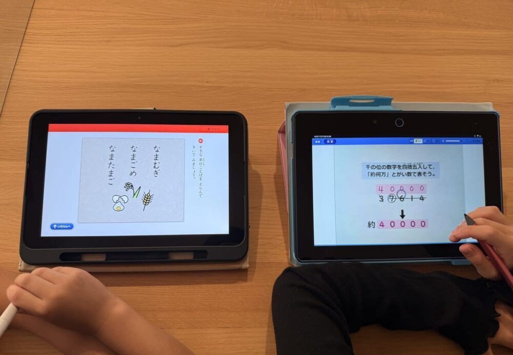 2台のタブレットで、きょうだいが並んで勉強しているところ(左がスマイルゼミ、右がチャレンジタッチ。手元だけ)